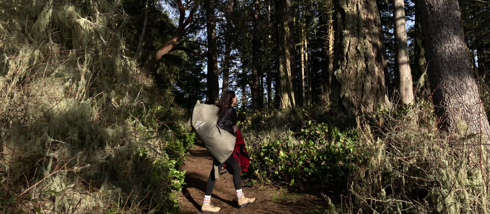 Person hiking through a forest trail carrying camping gear