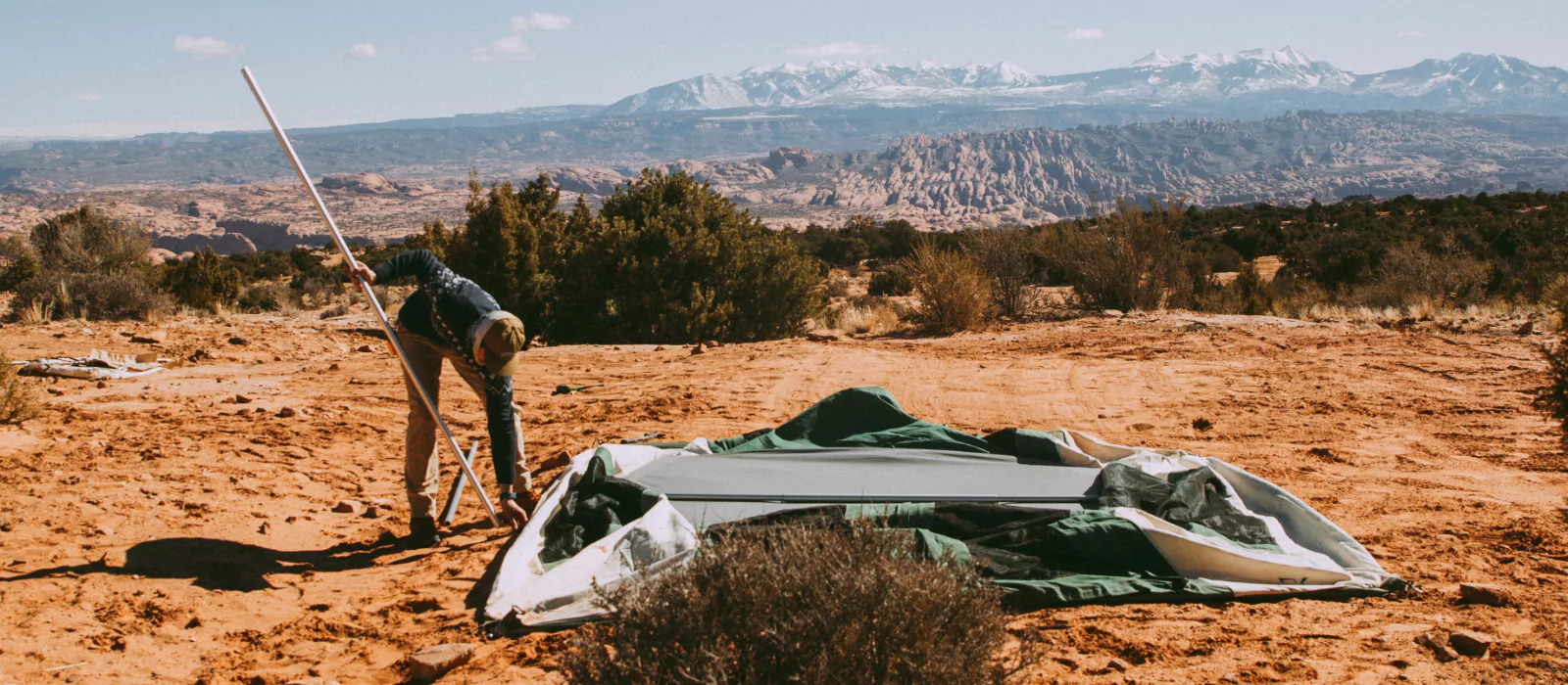 Camper setting up a cabin tent on a desert terrain with mountains in the background.