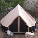 Canvas tent set up in a forested outdoor campsite with a white dog resting on a dog bed—perfect for pet-friendly camping.