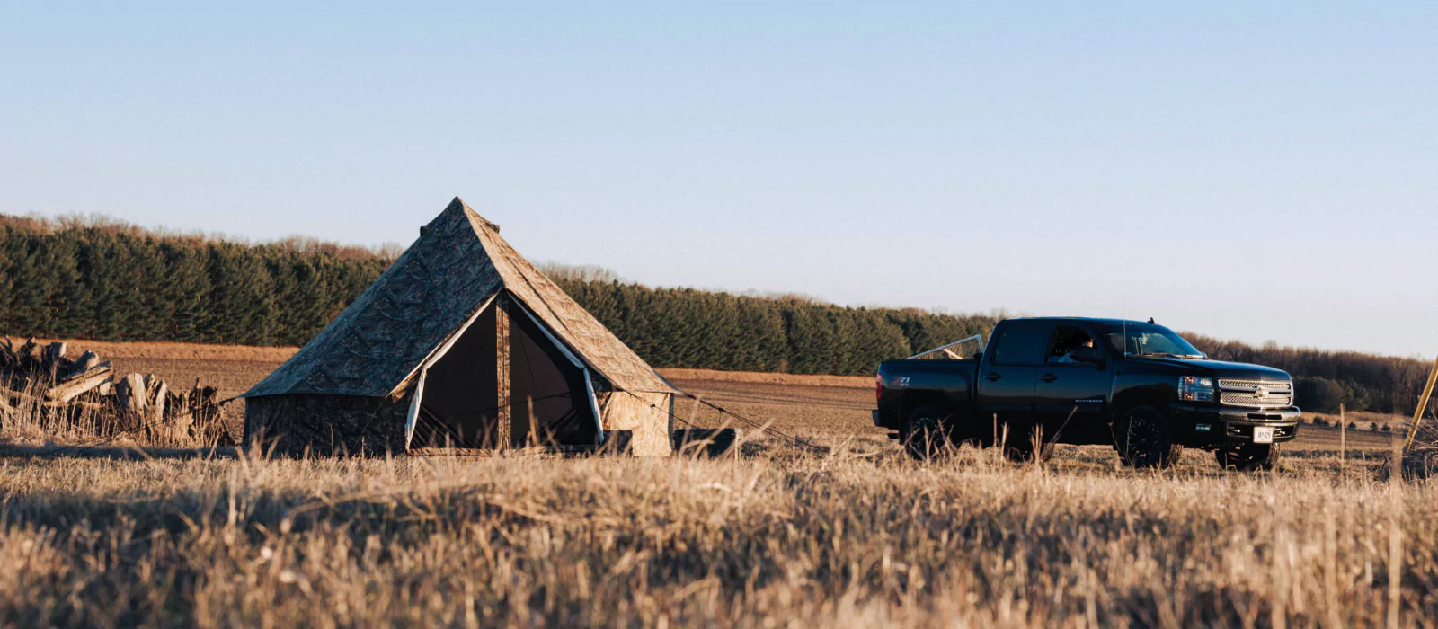 A canvas tent set up in a field next to a black pickup truck at a peaceful campsite surrounded by trees and open land.
