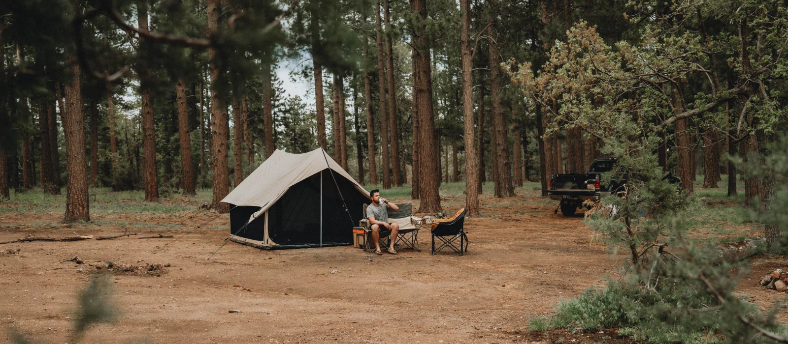 Man relaxing outside a canvas tent in a shaded forest campsite, demonstrating how to stay cool while camping in hot weather without A/C