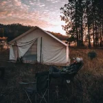 Campers relaxing outside a canvas tent during sunset on a quiet, crowd-free camping trip in the forest