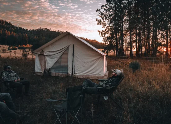 Campers relaxing outside a canvas tent during sunset on a quiet, crowd-free camping trip in the forest