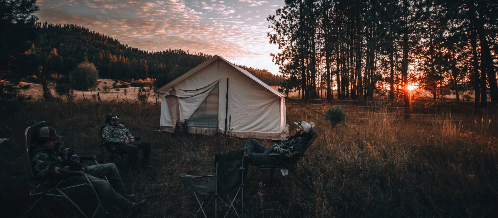 Campers relaxing outside a canvas tent during sunset on a quiet, crowd-free camping trip in the forest