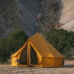 Bright yellow canvas tent set up in a remote desert landscape, surrounded by rocky hills and sparse vegetation.