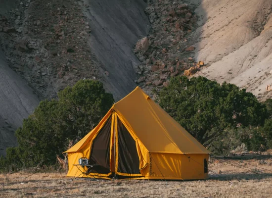 Bright yellow canvas tent set up in a remote desert landscape, surrounded by rocky hills and sparse vegetation.
