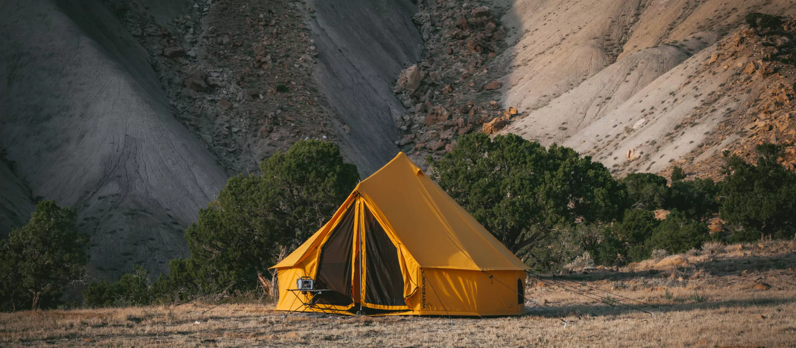 Bright yellow canvas tent set up in a remote desert landscape, surrounded by rocky hills and sparse vegetation.