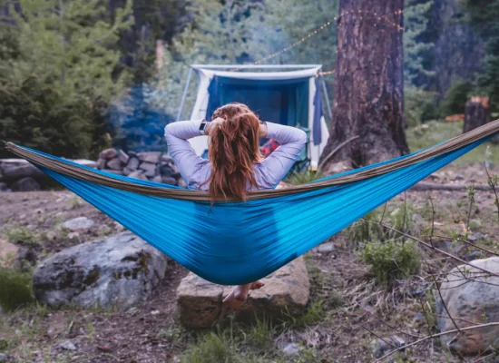 Person relaxing in a blue hammock between trees at a forest campsite, embracing nature for wellness and forest bathing benefits.
