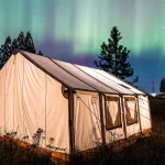 Canvas tent glowing at night under northern lights during a summer camping trip