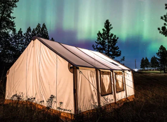 Canvas tent glowing at night under northern lights during a summer camping trip