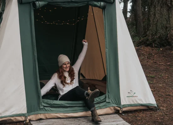 Woman stretching in the morning outside a canvas tent, ready for a restful day after a good night’s sleep while camping.