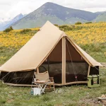 Canvas tent set up on a scenic mountain campground surrounded by wildflowers and green hills