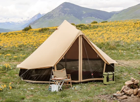 Canvas tent set up on a scenic mountain campground surrounded by wildflowers and green hills