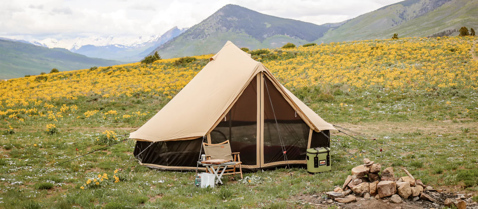 Canvas tent set up on a scenic mountain campground surrounded by wildflowers and green hills