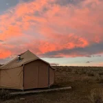 A bell tent set up for fall camping in an open field beneath a vibrant pink and orange sunset sky.