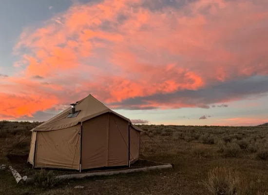 A bell tent set up for fall camping in an open field beneath a vibrant pink and orange sunset sky.