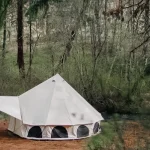 Canvas bell tent set up in a forest clearing for peaceful summer forest camping.