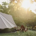 Canvas bell tent set up in a sunny clearing with trees around, ideal for hot weather camping in summer
