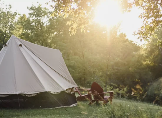 Canvas bell tent set up in a sunny clearing with trees around, ideal for hot weather camping in summer