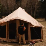 Person standing outside a canvas tent while camping in Colorado mountains surrounded by trees