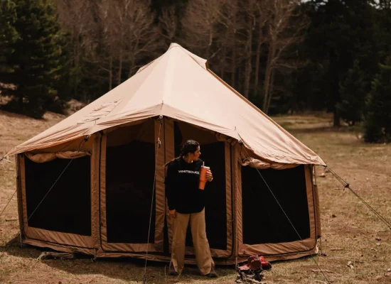 Person standing outside a canvas tent while camping in Colorado mountains surrounded by trees