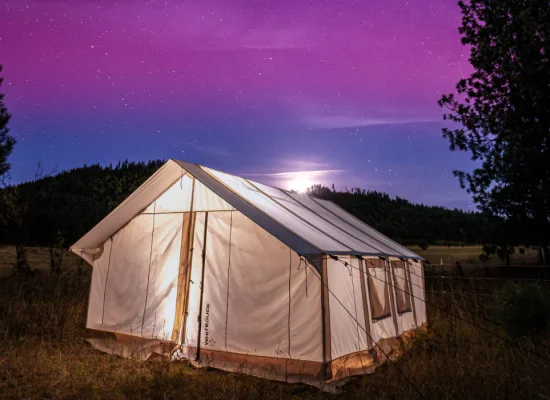 A glowing wall tent set up under a starry night sky, surrounded by trees and mountains, perfect for camping in Florida.