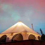 A glowing bell tent set against a colorful evening sky and forested mountains, creating a serene camping in Utah experience.