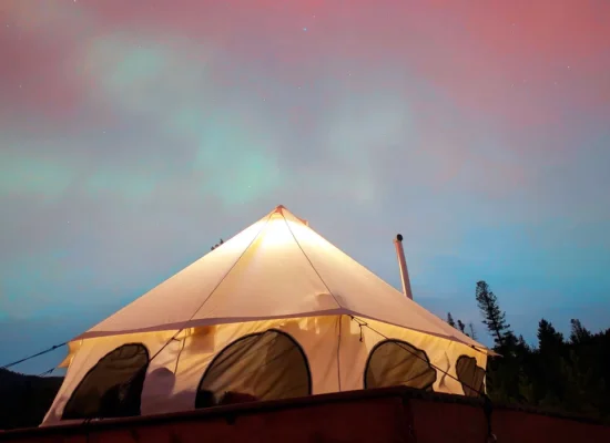 A glowing bell tent set against a colorful evening sky and forested mountains, creating a serene camping in Utah experience.