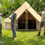 Group of friends camping in Washington with a canvas tent set up in a grassy field surrounded by forest.