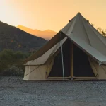Large canvas tent set up in a desert landscape at sunset with mountains in the background.