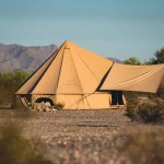 Canvas bell tent set up in the Arizona desert with mountains and cactus in the background.