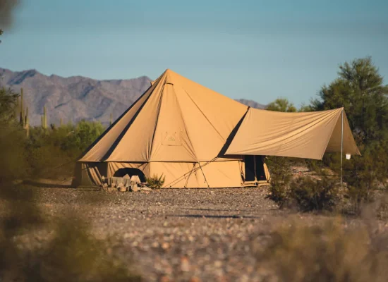 Canvas bell tent set up in the Arizona desert with mountains and cactus in the background.