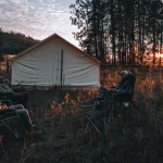 Friends camping in front of a canvas tent at sunset in the woods