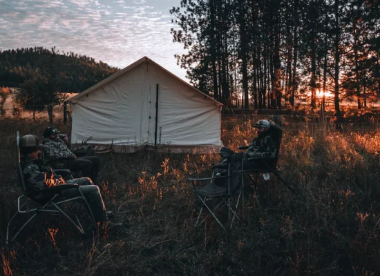 Friends camping in front of a canvas tent at sunset in the woods