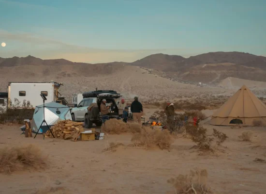 Group camping in Oregon desert with canvas tent, campfire, and vehicles under mountain sunset.