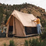 Camper setting up a canvas tent in a scenic Texas campsite surrounded by hills and greenery
