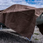 Brown canvas tarp covering a boat on a trailer outdoors