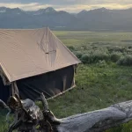 Canvas tent set up on grassy field with mountain views and ATV nearby