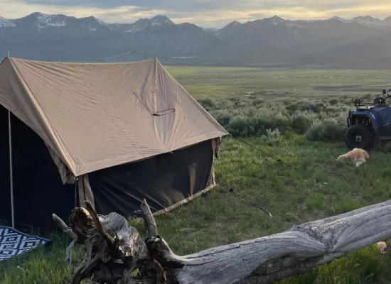 Canvas tent set up on grassy field with mountain views and ATV nearby