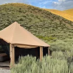 A canvas tent set up in scenic grassy hills during fall camping, surrounded by golden autumn light and peaceful nature.