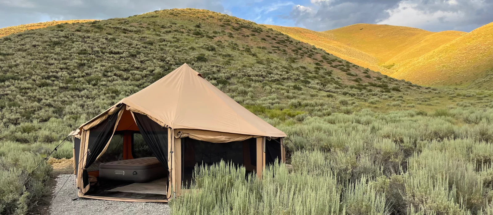 A canvas tent set up in scenic grassy hills during fall camping, surrounded by golden autumn light and peaceful nature.