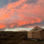 Canvas tent set up during fall camping under a colorful sunset sky
