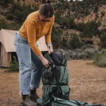 Camper packing gear near a tent in the outdoors, showcasing essential fall camping gear.