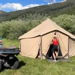 Family camping in a canvas tent with ATV in a grassy meadow during fall