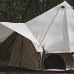 Canvas hunting camp tent with tarp extension set up in the woods