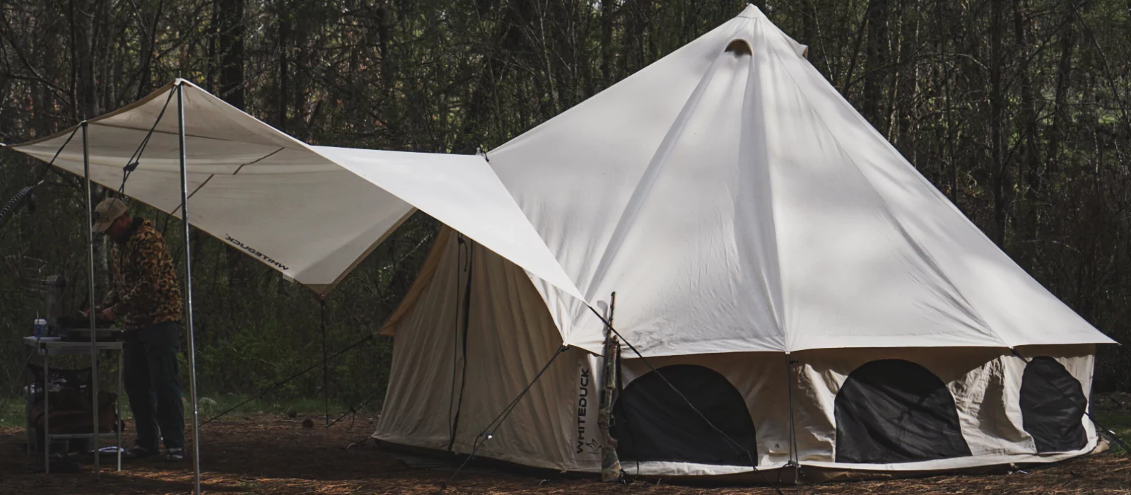 Canvas hunting camp tent with tarp extension set up in the woods
