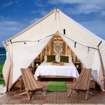 Luxury glamping tent set up on a beach with wooden flooring, cozy bed, and chairs showcasing stylish tent flooring ideas.