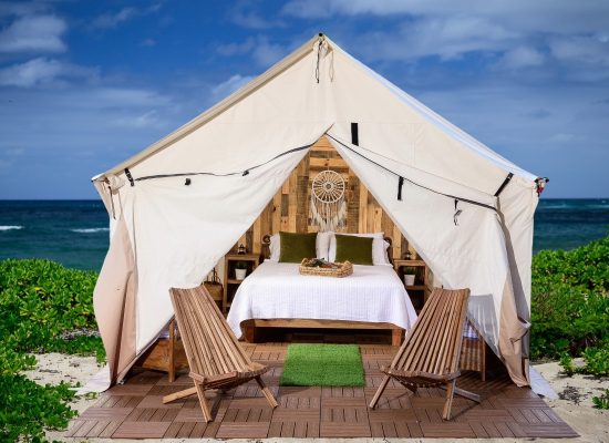 Luxury glamping tent set up on a beach with wooden flooring, cozy bed, and chairs showcasing stylish tent flooring ideas.