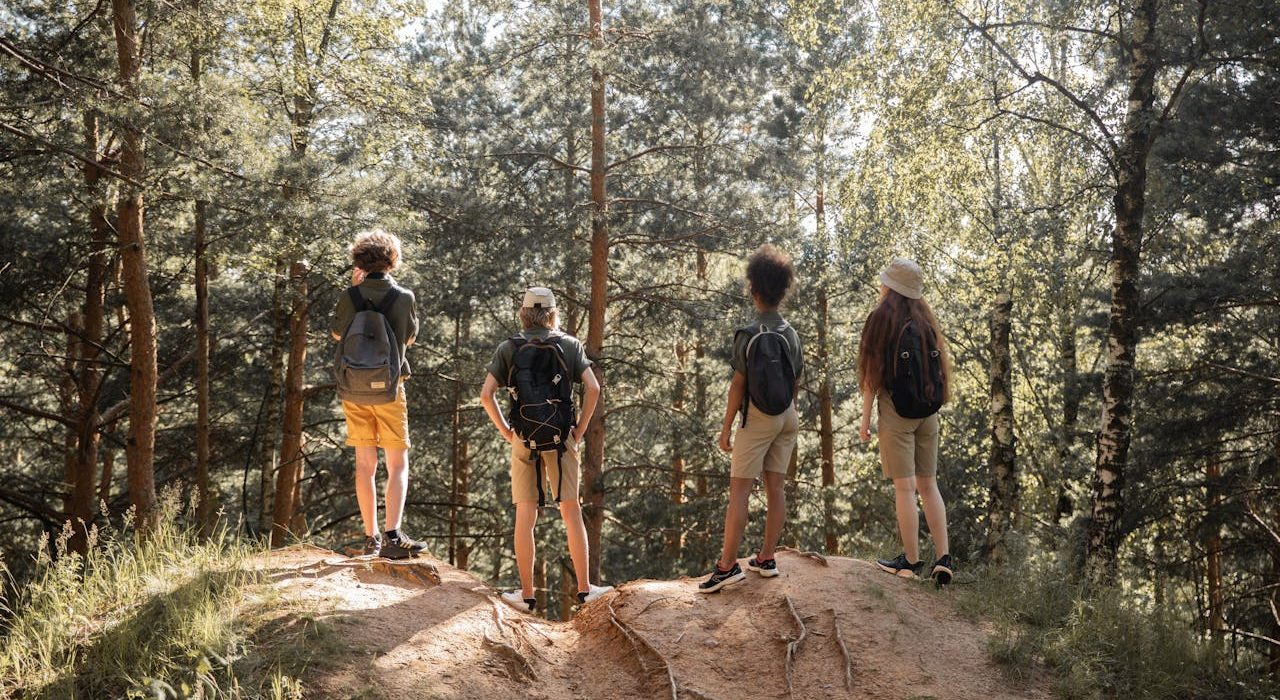Four young people with backpacks stand on a hilltop in the forest, bonding with nature during a hike. Photo by Ekaterina Bolovtsova on Pexels.