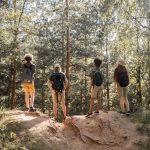 Four young people with backpacks stand on a hilltop in the forest, bonding with nature during a hike. Photo by Ekaterina Bolovtsova on Pexels.